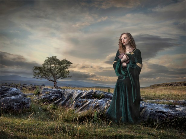 Girl in green robw with bible in limestone landscape with lone tree